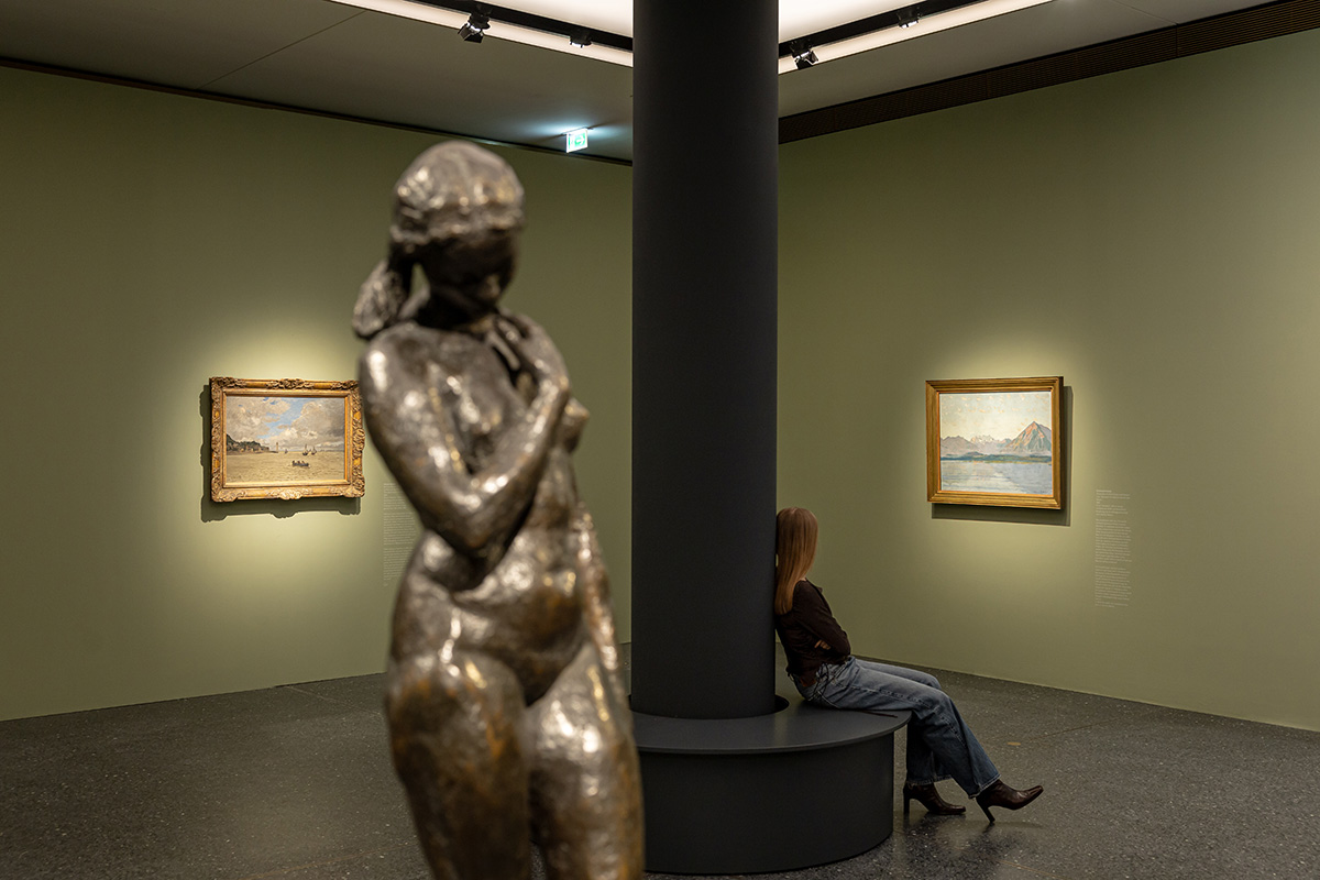 Auf dem Bild sieht man eine Skulptur in der Ausstellung Von Monet bis Picasso. Jüdische Kunstsammler:innen in Deutschland. Im Hintergrund sind zwei Werke sowie eine sitzende Person in der Ausstellung zu erkennen. 