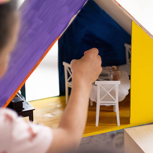 Das Bild zeigt ein Kind. Das Kind baut ein Modellzimmer.
