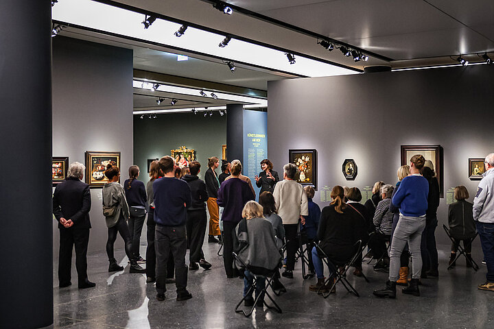Auf dem Bild sind viele Personen im Ausstellungraum zu sehen. Sie werden von einem Guide durch die Ausstellung geführt.