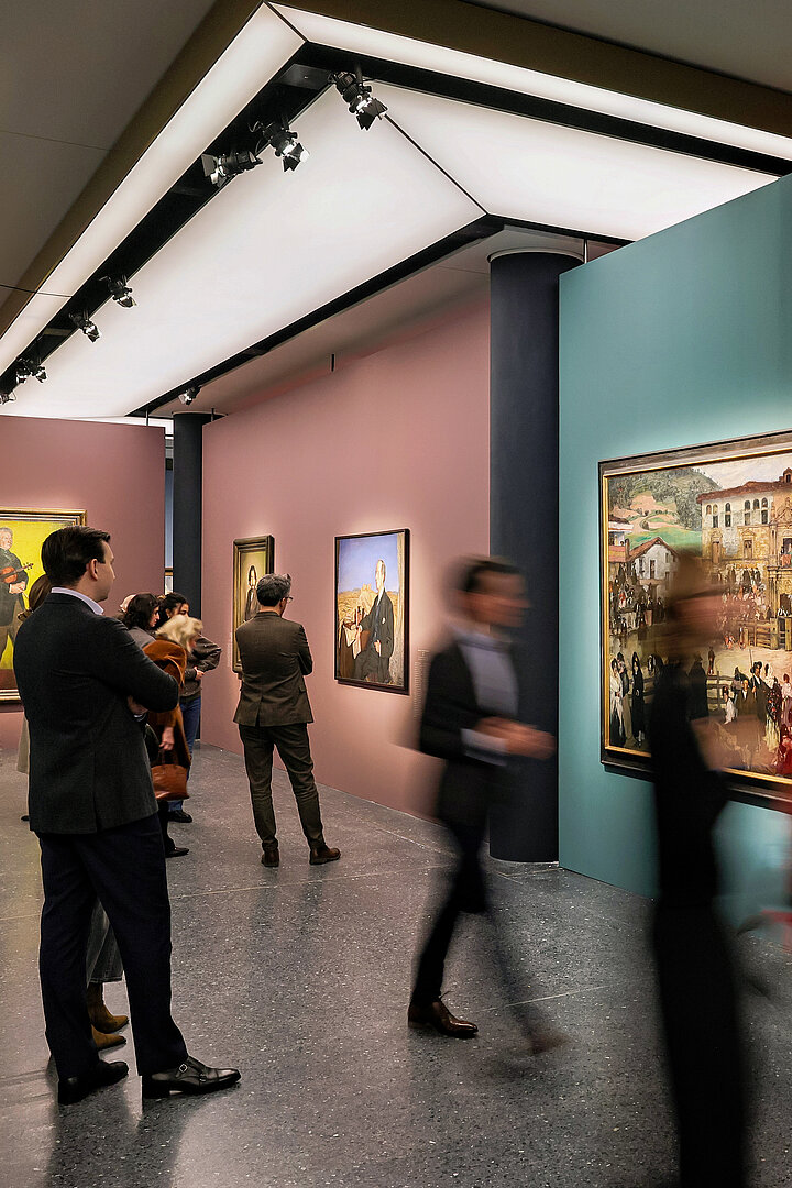 Auf dem Bild sind Personen im Ausstellungraum zu sehen. Sie unterhalten sich und schauen sich Gemälde an.