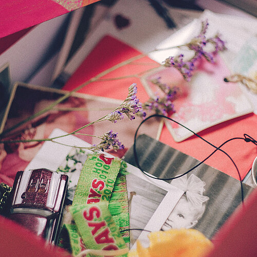 Das Bild zeigt einen roten Koffer mit Briefen, Blumen und Dekoartikeln.