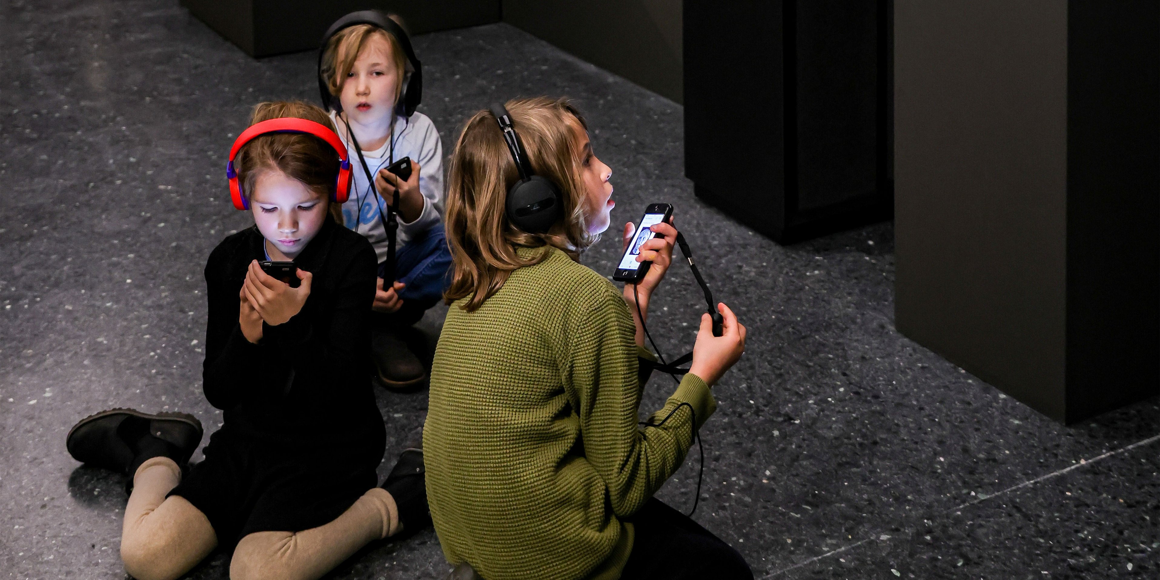 Kinder sitzen auf dem Boden und hören den Audioguide