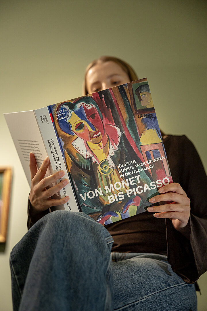 Person mit Ausstellungskatalog. Die Person liest in einem Katalog zur Ausstellung "Von Monet bis Picasso"